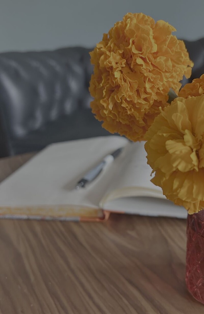 An open notebook and pen on a table, with flowers in the foreground.